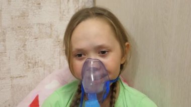 Tabletli çocuk hasta ve astım spreyinden nefes alıyor. Yakın plan. Hastanede yüzünde solunum maskesiyle tedavi edilen küçük bir kız. Yürümeye başlayan çocuk, solunum buharı soluyarak grip tedavisi görüyor..