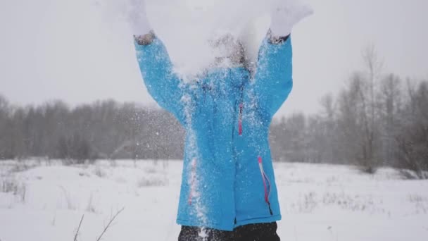 幸せな女性は森の中で手で雪を投げる。雪が降り、太陽の下で輝きます。クリスマス休暇のために公園で冬に遊ぶ女の子. — ストック動画