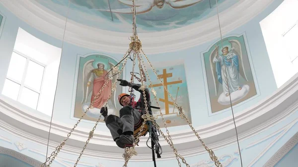 Escalade industrielle dans des équipements pour le travail en haute altitude travaillant à haute altitude dans un bâtiment d'église. Installation en haute altitude d'un lustre et d'un éclairage. sur les mousquetons de ceinture du grimpeur . — Photo