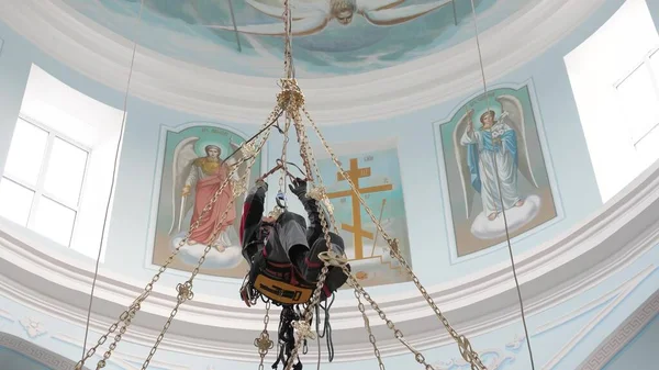 Industrial climber in equipment for high-altitude work working at high altitude in a church building. Climber high-altitude installation of a chandelier and lighting. on the climber s belt carabiners.