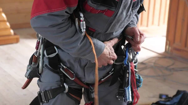 industrial climber puts on equipment for high-altitude work. on the climber s belt carabiners.