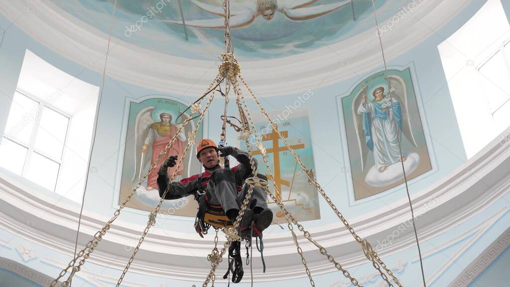 Industrial climber in equipment for high-altitude work working at high altitude in a church building. Climber high-altitude installation of a chandelier and lighting. on the climber s belt carabiners.