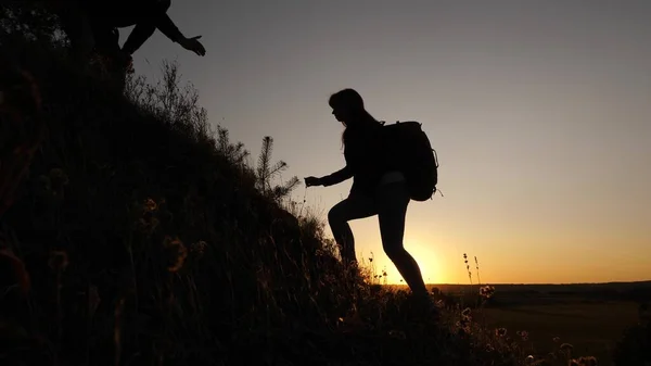 Una turista donna tiene per mano un viaggiatore maschio che aiuta a scalare la cima della collina. I turisti scalano la montagna al tramonto, tenendosi per mano. Lavoro di squadra di soci in affari. Famiglia felice in vacanza — Foto Stock