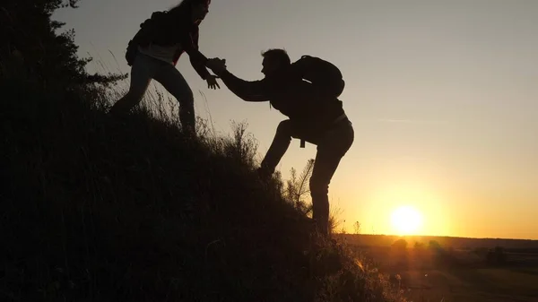 Ein männlicher Reisender reicht einer Reisenden die Hand, die einen Hügel erklimmt. Touristen erklimmen den Berg im Sonnenuntergang, Händchen haltend. Teamwork der Geschäftsleute. glückliche Familie im Urlaub. — Stockfoto