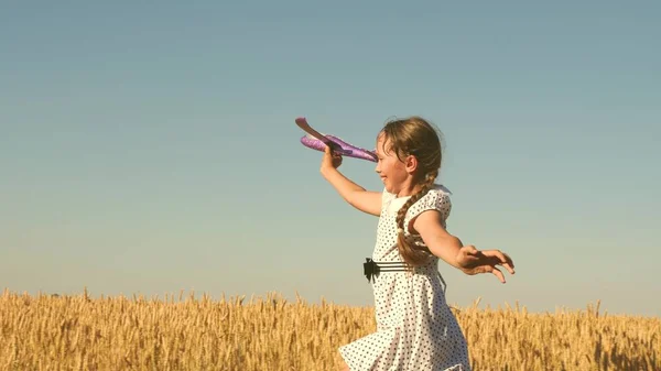 Счастливая девушка бежит с игрушечным самолетом на поле при закате солнца. Дети играют в игрушечный самолет. подросток мечтает летать и стать пилотом. Девушка хочет стать пилотом и астронавтом. Медленное движение — стоковое фото