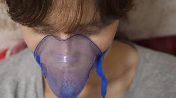 Une fille malade dans un masque respire un vaporisateur. Femme avec un masque bleu d'hôpital. Inspirez des vapeurs des voies respiratoires dans les poumons. Traitement de la toux. Gros plan — Photo