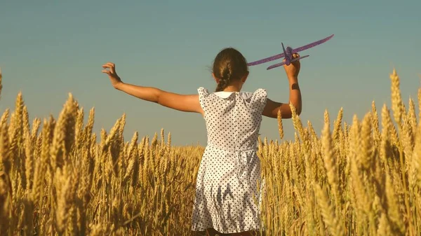 Glückliches Mädchen rennt mit einem Spielzeugflugzeug auf einem Feld im Sonnenuntergang. Kinder spielen Spielzeugflugzeug. Teenager träumt davon zu fliegen und Pilot zu werden. Das Mädchen will Pilotin und Astronautin werden. Zeitlupe — Stockfoto