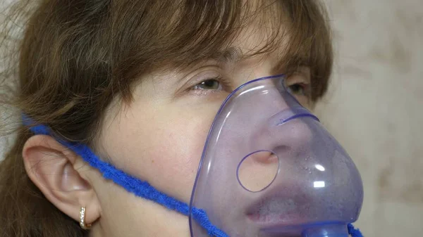 woman is treated with an inhalation mask on her face in a hospital. sick girl is inhaled by a nebulizer sitting on sofa. woman in mask. Inhale vapors for respiratory tract into lungs. Cough treatment