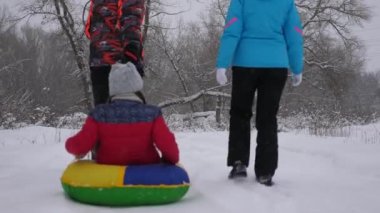 Annem ve babam kızlarını kış ormanında kızakla gezdiriyorlar. Mutlu ebeveynler Noel parkında çocuklarıyla oynarlar. Aile Noel tatili için bir kış parkında oynar. Yavaş çekim.