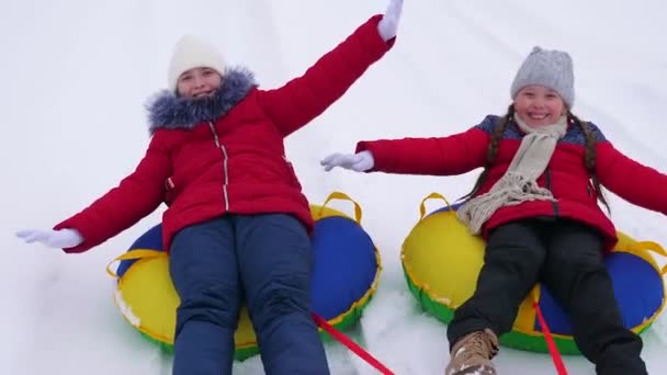 Happy childhood concept. Childrens Christmas holidays outdoors. Happy children have fun riding snow saucer and laugh on snowy winter road on winter frosty day. Teens play on sled in winter field and — ストック動画