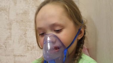 Tabletli çocuk hasta ve astım spreyinden nefes alıyor. Yakın plan. Hastanede yüzünde solunum maskesiyle tedavi edilen küçük bir kız. Yürümeye başlayan çocuk, solunum buharı soluyarak grip tedavisi görüyor..