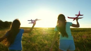 Uçma hayalleri. Mutlu çocukluk kavramı. Gün batımında iki kız bir oyuncak uçakla oynuyor. Güneşin arka planındaki çocuklar ellerinde bir uçakla. Uçakta oynayan çocukların silueti.