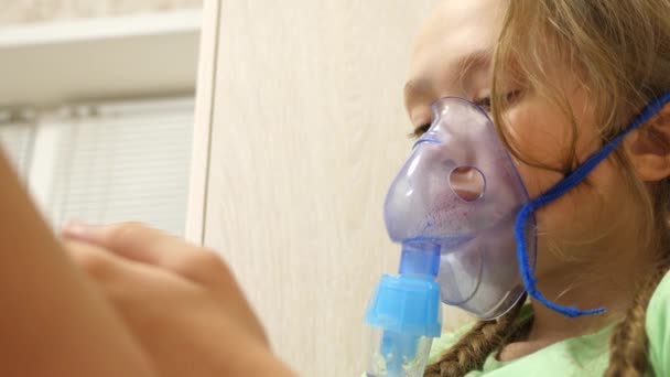 El niño con el comprimido está enfermo y respira a través de un inhalador. Primer plano. niña pequeña tratada con una máscara de inhalación en su cara en el hospital. El niño pequeño trata la gripe inhalando vapor de inhalación . — Vídeo de stock