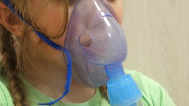 El niño con el comprimido está enfermo y respira a través de un inhalador. Primer plano. niña pequeña tratada con una máscara de inhalación en su cara en el hospital. El niño pequeño trata la gripe inhalando vapor de inhalación . — Vídeo de stock