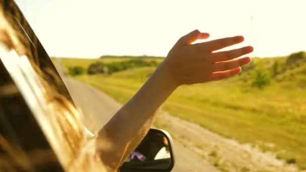 Menina com cabelos longos está sentado no banco da frente do carro, esticando o braço para fora da janela e pegando o brilho do pôr-do-sol — Vídeo de Stock