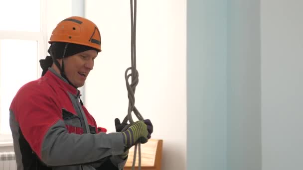 Промышленный альпинист вяжет веревку для подъемного оборудования. рабочий в защитном шлеме вяжет узел на веревке . — стоковое видео