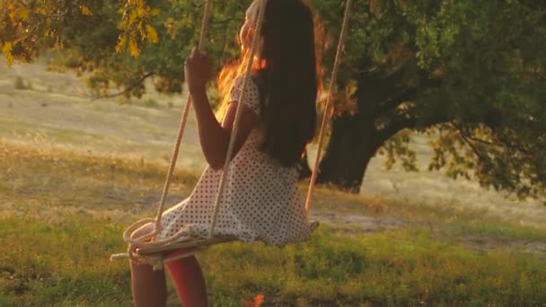 Dítě houpající se na houpačce v parku na slunci. mladá dívka houpající se na provaze na dubové větvi. dospívající dívka má rád let na houpačce v létě večer v lese. koncept šťastné rodiny a dětství. — Stock video