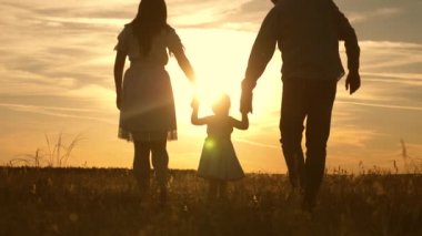 Mutlu bebek ve ebeveynler gün batımında yürüyecekler. Güneşin altında yürüyen bir ailenin silueti. Anne, baba ve çocuk. Mutlu aile kavramı. Aile yaşam tarzı