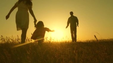 Mutlu çocuk ve ebeveynler gün batımında yürürler. Babam kızına sarılıyor ve uçarken fırıl fırıl dönüyor. Güneşin altında yürüyen bir ailenin silueti. Anne, baba ve bebek. Mutlu aile kavramı. Aile yaşam tarzı