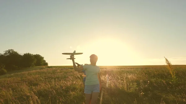 Sueños de volar. Concepto de infancia feliz. Dos chicas juegan con un avión de juguete al atardecer. Niños en el fondo del sol con un avión en la mano. Silueta de niños jugando en el avión —  Fotos de Stock