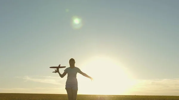 Счастливая девушка бежит с игрушечным самолетом на поле при закате солнца. Дети играют в игрушечный самолет. подросток мечтает летать и стать пилотом. Девушка хочет стать пилотом и астронавтом. Медленное движение — стоковое фото