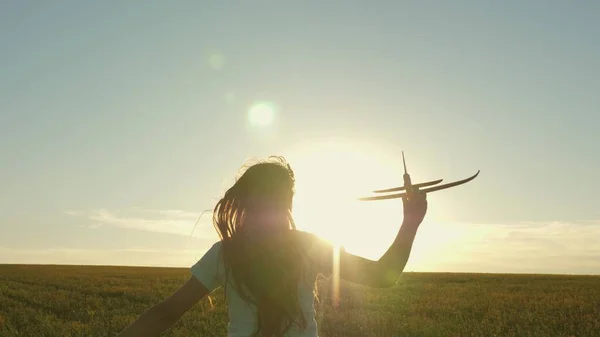 Happy girl runs with a toy airplane on a field in the sunset light. children play toy airplane. teenager dreams of flying and becoming pilot. the girl wants to become pilot and astronaut. Slow motion