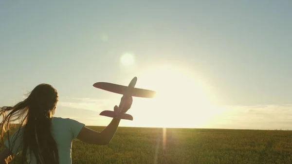 Glückliches Mädchen rennt mit einem Spielzeugflugzeug auf einem Feld im Sonnenuntergang. Kinder spielen Spielzeugflugzeug. Teenager träumt davon zu fliegen und Pilot zu werden. Das Mädchen will Pilotin und Astronautin werden. Zeitlupe — Stockfoto