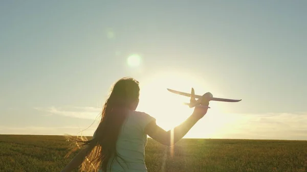 在夕阳西下，快乐的女孩带着一架玩具飞机在田野里奔跑。孩子们玩玩具飞机。青少年的梦想是飞行和成为飞行员。这个女孩想成为一名飞行员和宇航员。慢动作 — 图库照片