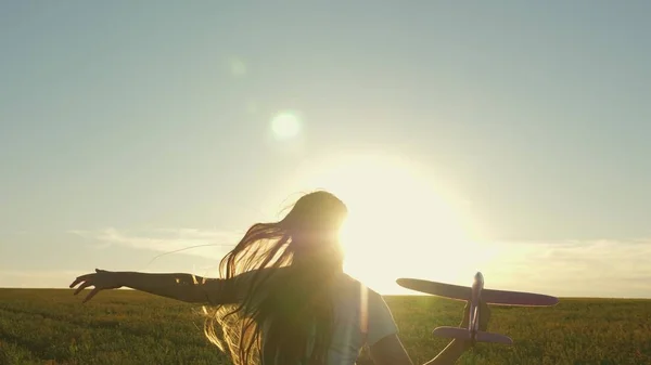 Menina feliz corre com um avião de brinquedo em um campo sob a luz do pôr do sol. As crianças brincam de avião de brinquedo. sonho adolescente de voar e se tornar piloto. a menina quer se tornar piloto e astronauta. Movimento lento — Fotografia de Stock