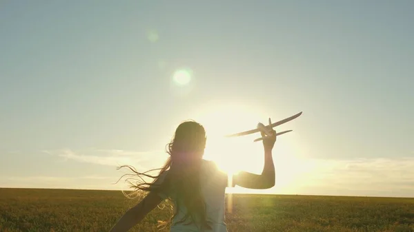 在夕阳西下，快乐的女孩带着一架玩具飞机在田野里奔跑。孩子们玩玩具飞机。青少年的梦想是飞行和成为飞行员。这个女孩想成为一名飞行员和宇航员。慢动作 — 图库照片
