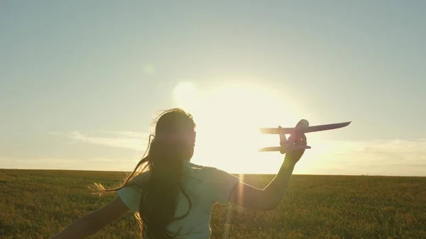 Lycklig flicka springer med ett leksaksplan på ett fält i solnedgångens sken. Barn leker leksaksflygplan. Tonåringen drömmer om att flyga och bli pilot. Flickan vill bli pilot och astronaut. Långsamma rörelser — Stockfoto