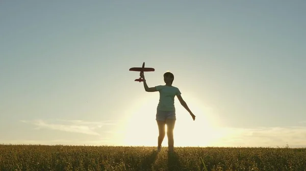 Ragazza felice corre con un aeroplano giocattolo su un campo alla luce del tramonto. i bambini giocano aereo giocattolo. adolescente sogna di volare e diventare pilota. la ragazza vuole diventare pilota e astronauta. Rallentatore — Foto Stock