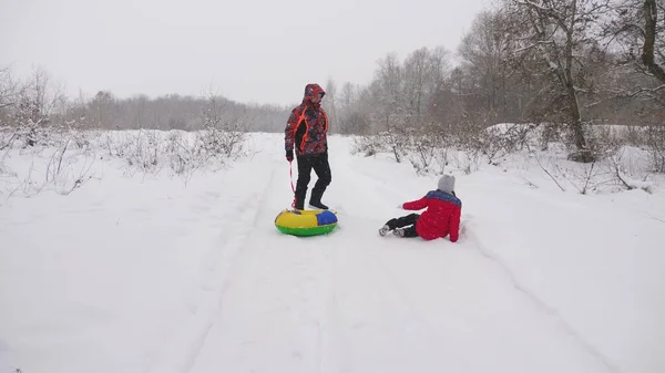 Glad pappa släpar ett barn på en snöig väg. Julhelger. Pappa leker med sin dotter i en vinterpark. Begreppet lycklig familj. En tonåring rider i Tubing — Stockfoto