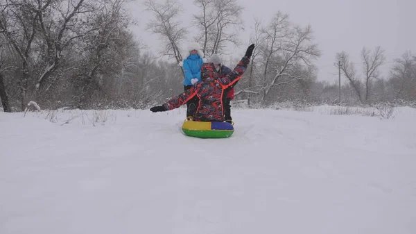 Mamma och dotter åker pulka pappa i vinterskogen, i snöfall. Glada föräldrar och barn leker i julparken. Familjen leker i vinterparken på julhelgen. — Stockfoto