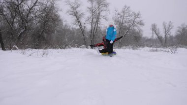 Anne ve kızı kış ormanlarında, kar yağarken kızak kayıyor. Mutlu ebeveynler ve bebek noel parkında oynuyorlar. Aile, Noel tatillerinde kış parkında oynar..