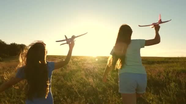 Dreams of flying. Happy childhood concept. Two girls play with a toy plane at sunset. Children on background of sun with an airplane in hand. Silhouette of children playing on the plane — Stock Video