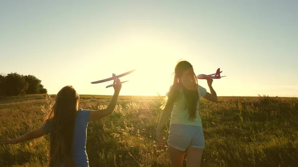 Träume vom Fliegen. Glückliche Kindheit. Zwei Mädchen spielen bei Sonnenuntergang mit einem Spielzeugflugzeug. Kinder im Hintergrund der Sonne mit einem Flugzeug in der Hand. Silhouette von Kindern, die im Flugzeug spielen — Stockfoto