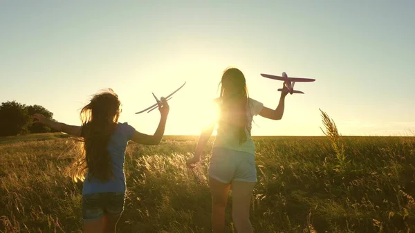 Sonhos de voar. Feliz conceito de infância. Duas raparigas brincam com um avião de brincar ao pôr-do-sol. Crianças no fundo do sol com um avião na mão. Silhueta de crianças brincando no avião — Fotografia de Stock