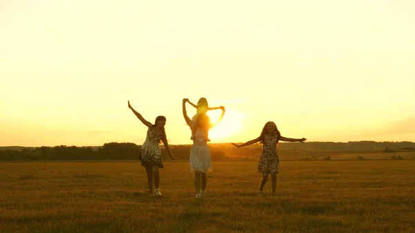 Concept d'enfance heureuse. Joyeux jeune famille avec un enfant courir à travers le champ en vol à la lumière du coucher du soleil. Mère et filles se promènent dans le parc et jouent dans la prairie au soleil. concept de vie d'une grande famille — Photo