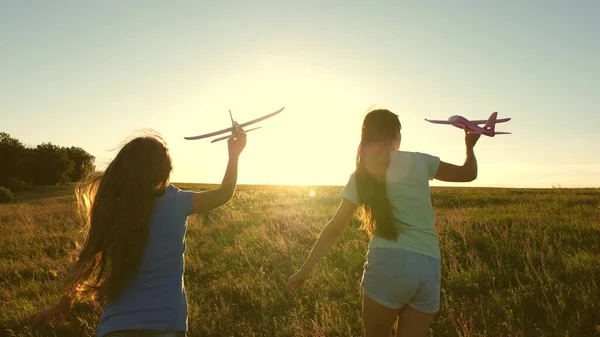 Sogni di volare. Concetto infanzia felice. Due ragazze giocano con un aereo giocattolo al tramonto. Bambini sullo sfondo del sole con un aereo in mano. Silhouette di bambini che giocano sull'aereo — Foto Stock