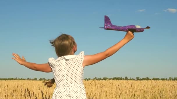 Szczęśliwa dziewczyna biegnie z zabawkowym samolotem na polu w świetle zachodu słońca. Dzieci bawią się w zabawkowy samolot. nastolatek marzy o lataniu i zostaniu pilotem. Dziewczyna chce zostać pilotem i astronautą. Zwolniony ruch — Wideo stockowe