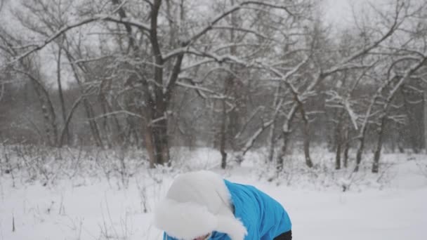 Kobieta gra zimą w parku na święta Bożego Narodzenia. Szczęśliwa dziewczyna rzuca śniegiem z rękami w górze w lesie i śmieje się. Śnieg pada i błyszczy w słońcu. — Wideo stockowe