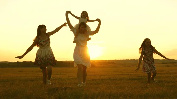 Concept d'enfance heureuse. Joyeux jeune famille avec un enfant courir à travers le champ en vol à la lumière du coucher du soleil. Mère et filles se promènent dans le parc et jouent dans la prairie au soleil. concept de vie d'une grande famille — Photo