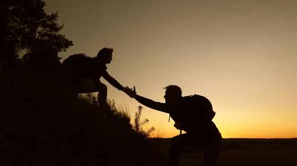 work in a team of climbers. female traveler holds hand of male traveler helping to climb top of hill. Tourists climb mountain at sunset, holding hands. team work of business partners.