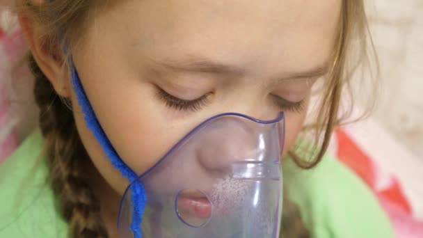 El niño con el comprimido está enfermo y respira a través de un inhalador. Primer plano. niña pequeña tratada con una máscara de inhalación en su cara en el hospital. El niño pequeño trata la gripe inhalando vapor de inhalación . — Vídeo de stock