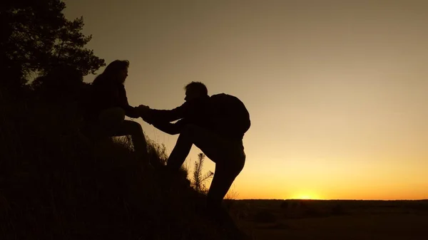 Work in a team of climbers. female traveler holds hand of male traveler helping to climb top of hill. Tourists climb mountain at sunset, holding hands. team work of business partners. — Stock Photo, Image