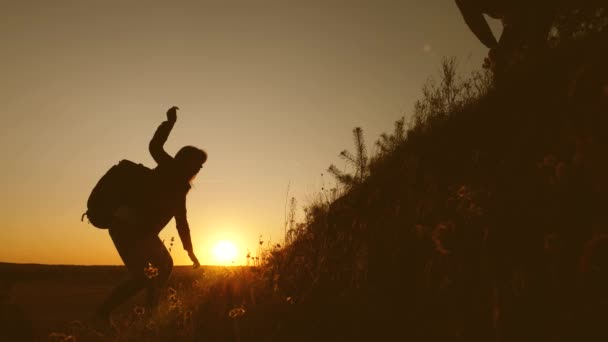 Los turistas suben a la montaña al atardecer, tomados de la mano. trabajo en equipo de gente de negocios. El viajero extiende una mano de mujer a un viajero que sube a la cima de la colina. Familia feliz de vacaciones . — Vídeos de Stock