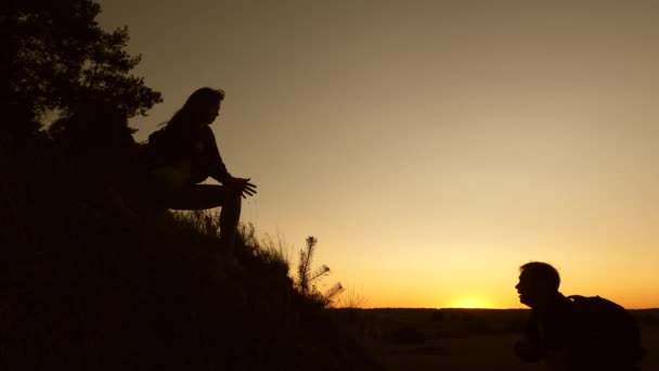 Work in a team of climbers. female traveler holds hand of male traveler helping to climb top of hill. Tourists climb mountain at sunset, holding hands. team work of business partners. — Stock Video