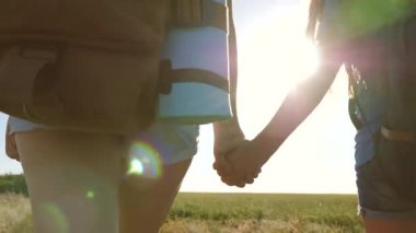 Kızlar, kadın gezginler el ele tutuşur. Yakın plan. Takım çalışması turistleri. Kadın gezginler kırsalda bir yolda yürürler. Yaz parkındaki mutlu yürüyüşçü kız. Kız gezginler sırt çantalarıyla gezerler.