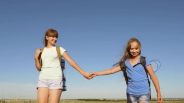Kızlar, kadın gezginler mavi gökyüzünün arka planında el ele tutuşurlar. Yakın plan. Takım çalışması turistleri. Kadın gezginler arazide yürür. Yazın çayırda yürüyüş yapan kızlar..